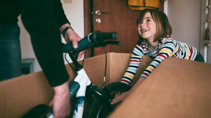 Kind öffnet freudestrahlend einen Karton, in dem ein Fahrrad drin ist